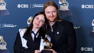 Eine junge Frau und ein junger Mann stehen nah beieinander und halten eine Trophäe in Form eines goldenen Grammophons.