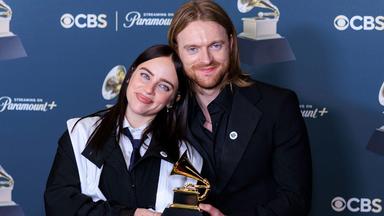 Eine junge Frau und ein junger Mann stehen nah beieinander und halten eine Trophäe in Form eines goldenen Grammophons.