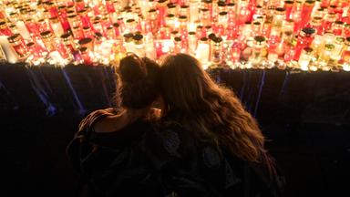 Zwei Frauen sitzen mit dem Rücken zur Kamera vor einem Meer aus Kerzen und stecken die Köpfe zusammen.