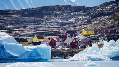 Grönland - zerstreut liegende bunte Holzhäuser vor kahlen Bergen mit Schnee.