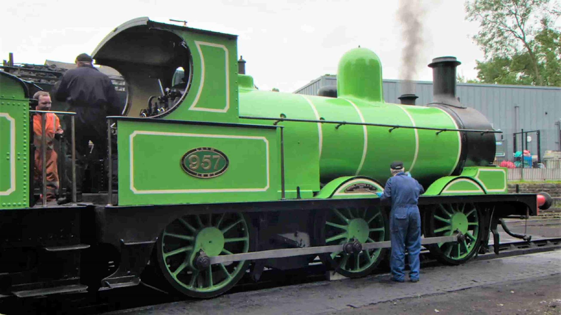 Drei Männer in Overalls arbeiten auf einem Bahnsteig an einer grünen Dampflokomotive.