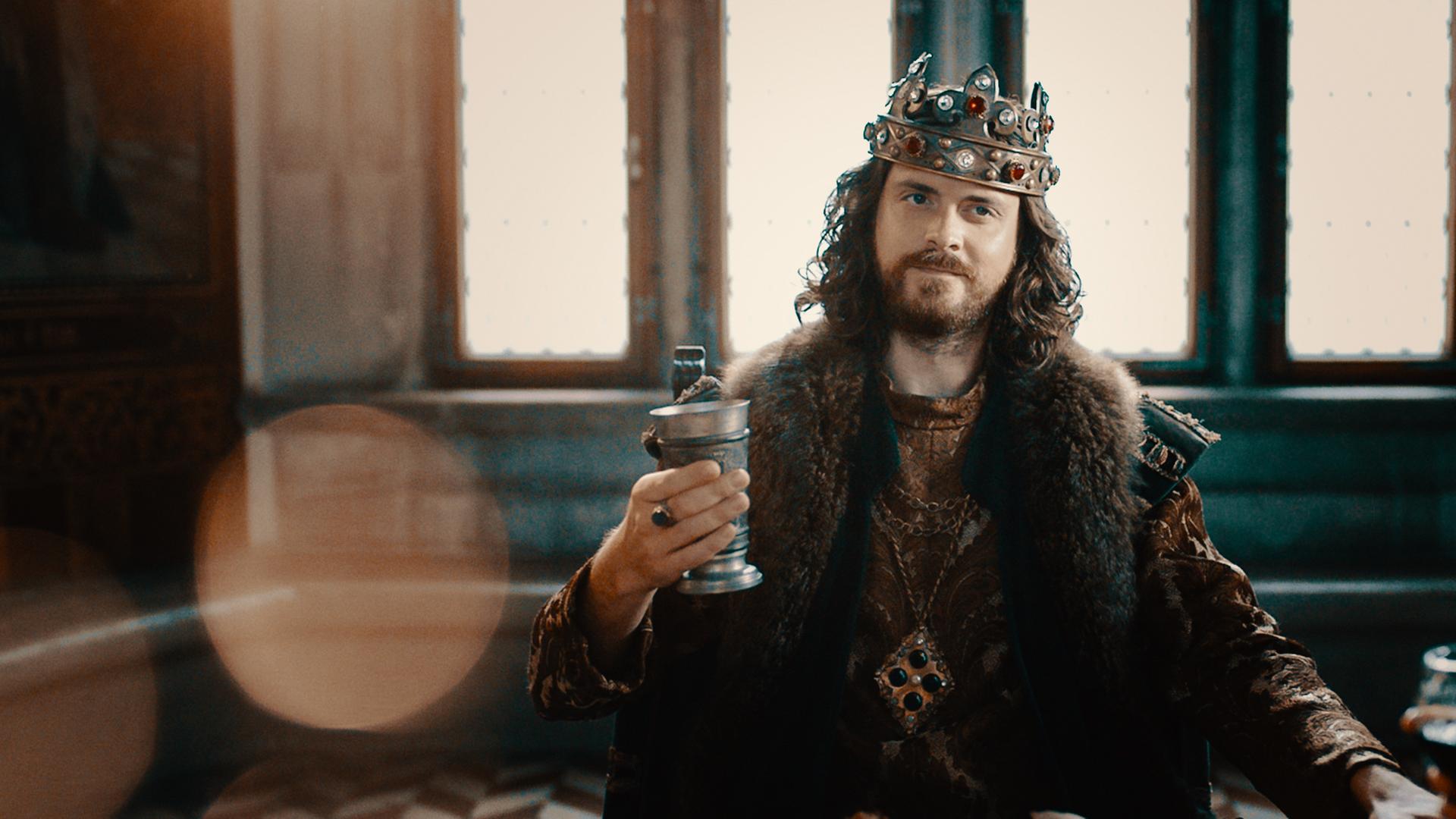 Spielszene. König Artus (Sebastian Fräsdorf) steht in seiner Garderobe und blickt kritisch in einen Spiegel.