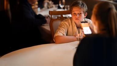 "Frühling - Gute Väter, schlechte Väter": Nicky Söringer (Valentin Wessely) sitzt in einem Restaurant an einem Tisch und blickt erwartungsvoll auf seine Schwester Paula (Lotte Hanné), die auf ihr Handy schaut.