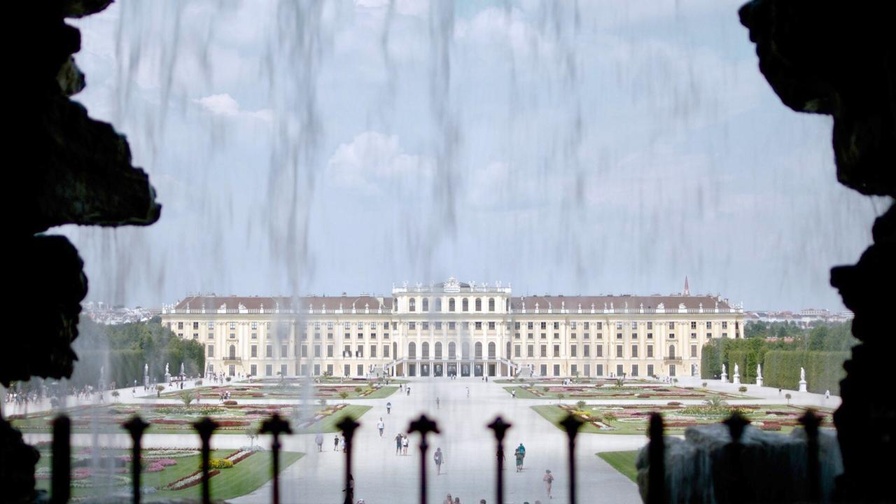 Blick durch Wasserkaskaden auf Schloss Schönbrunn in Wien, mit symmetrischen Gärten und dem imposanten Palast im Hintergrund