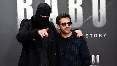 Ein Mann mit schwarzer Skimaske und ein zweiter stehen vor Filmwerbung.