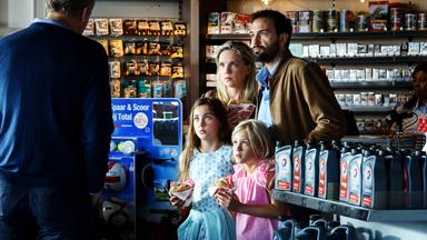 Ed (Willem de Wolf) ist nur von der Rückseite zu sehen und hat beide Hände in der Hosentasche versteckt. Robine (Liz Vergeer) und Milou (Roosmarijn van der Hoek) halten beide ein Sandwich in der Hand und blicken in leicht gebeugter Haltung verängstigt in Eds Richtung. Hans (Jeroen Spitzenberger), der neben seiner Frau und hinter beiden Töchtern steht, hält seine linke Hand beschützend um Robines linke Schulter. Diana hält ebenfalls ein Brötchen in der Hand und sieht Ed schockiert an.