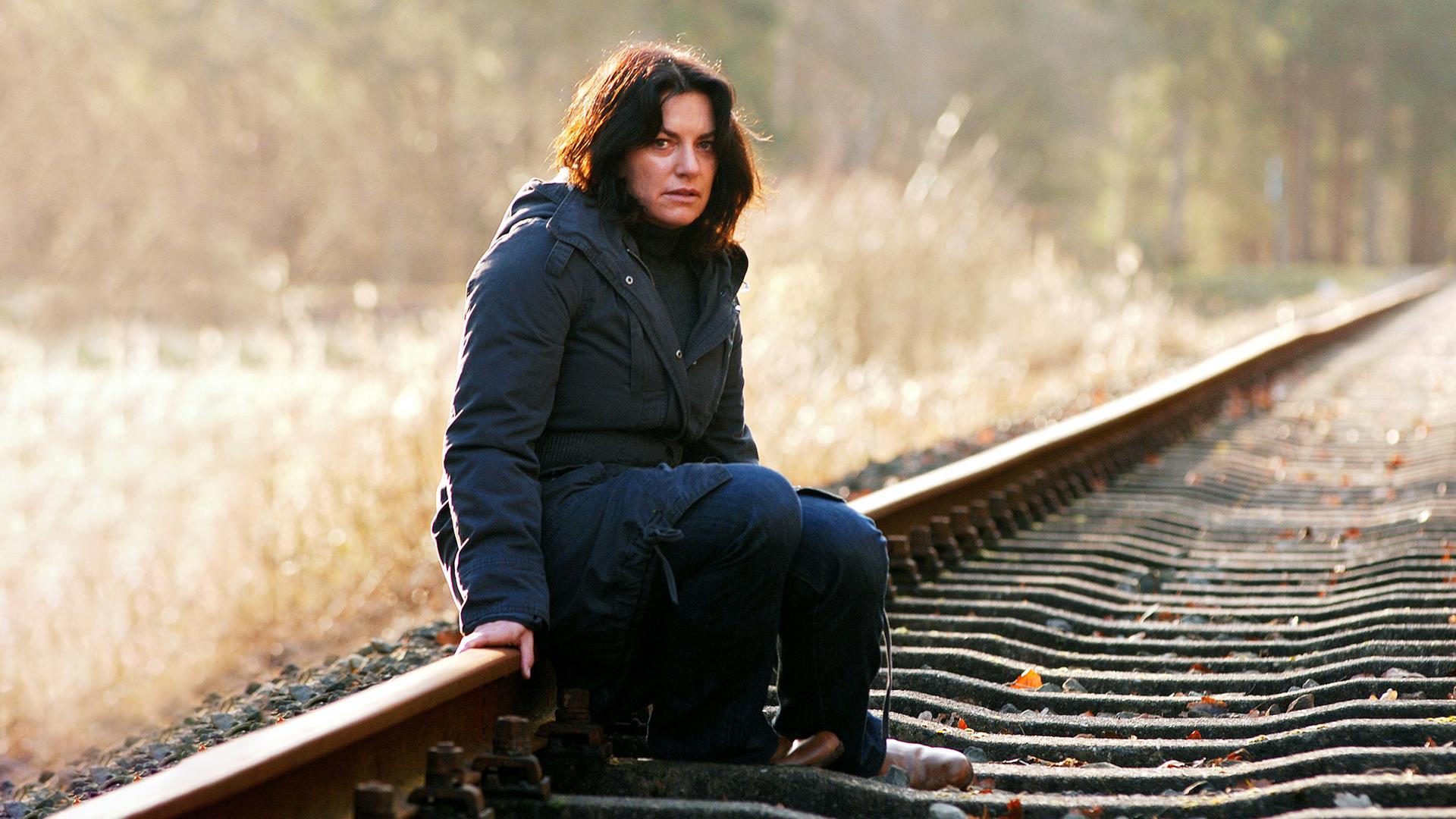 Eine Frau sitzt in einem dicken Mantel auf einer Bahnschiene