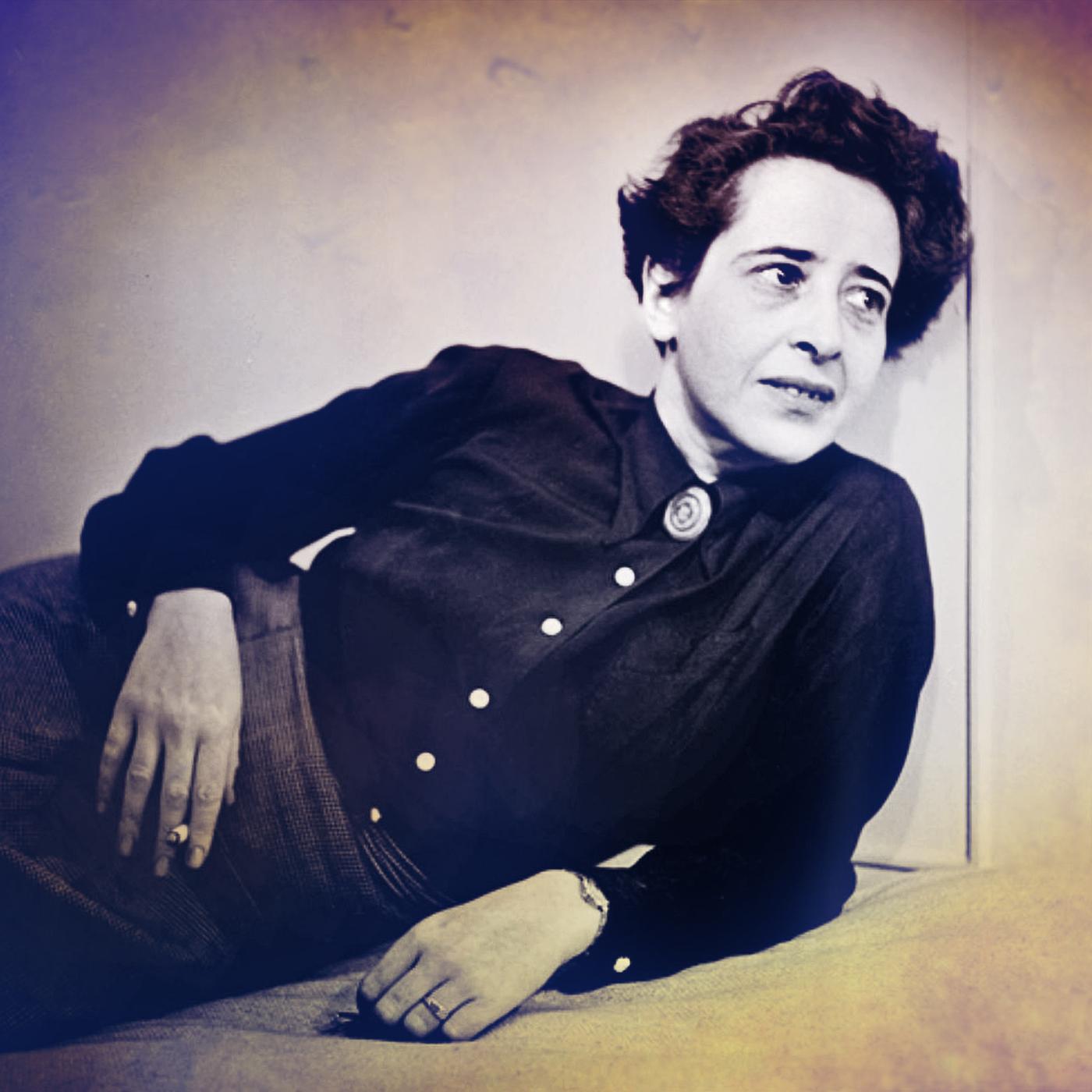 Hannah Arendt sitzt auf einem Sessel bei einem Fernsehinterview. Sie trägt ein schwarzes Kostüm und ihr Ellenbogen stützt sie auf der Armlehne auf. IN der Hand hält sie eine ZIgarette. Das Bild ist schwarz weiß. 