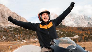 Ein junger Mann auf einem Motorrad streckt die Arme in die Luft.