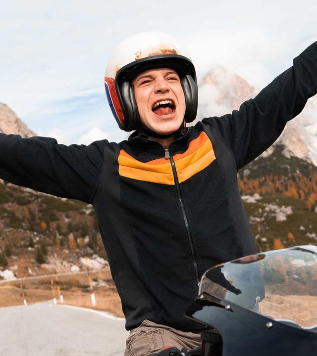 Ein junger Mann auf einem Motorrad streckt die Arme in die Luft.