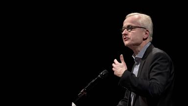 Ein Mann im Anzug spricht in ein Mikrofon.