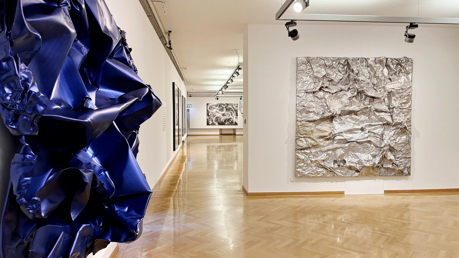 Zerknautschte Wandbilder aus Aluminium hängen in einem Ausstellungsraum