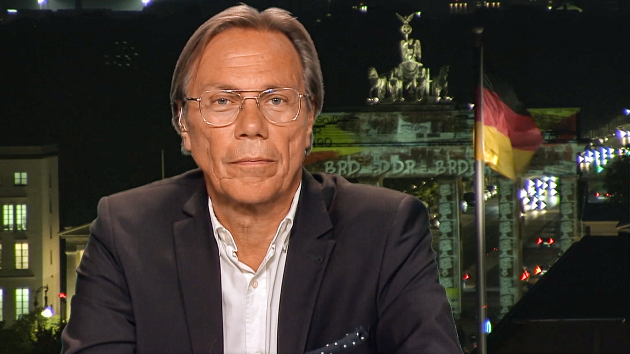 Ein Mann mit Anzug und Brille vor dem Hintergrund des Brandenburger Tors in Berlin