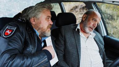 Koops (Aljoscha Stadelmann, li.) sitzt im Auto und blickt auf den sterbenden Schürer (Heinrich Cuipers) mit einem Kopfschuss.