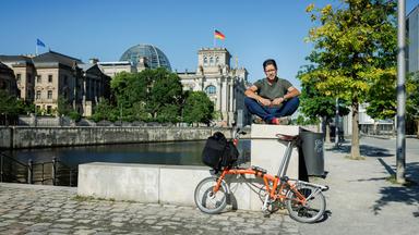 Mann sitzt auf Mauer vor dem Bundestag in Berlin.