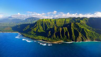 Luftaufnahme der spektakulären Na Pali Küste auf der Insel Kauai, Hawaii, mit grünen Bergen und dem blauen Meer.