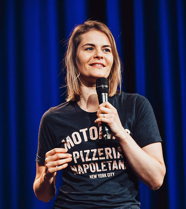 Hazel Brugger steht auf der Bühne vor einem blauen Vorhang.