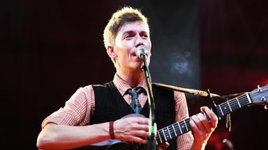 Nahaufnahme eines gitarrespielenden Mannes, der in ein Mikrofon singt.