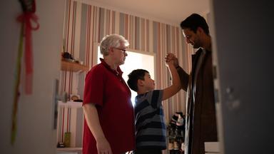 Samuel Sindhu gibt einem Jungen High five, der mit ihm und einem älteren Mann zusammen in einem Zimmer steht.
