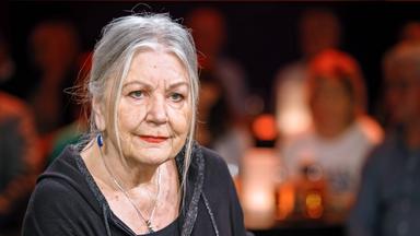 Porträtfoto einer älteren Frau mit zurückgebundenen langen grauen Haaren.