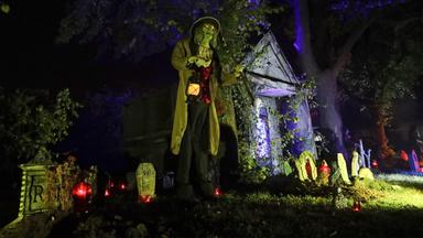 Helloween-Deko mit Geistern, Grabsteinen und einer Person mit Lampe