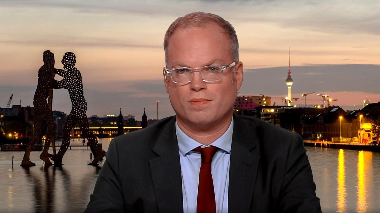 Mann mit Brille und Anzug vor Berliner Skyline.