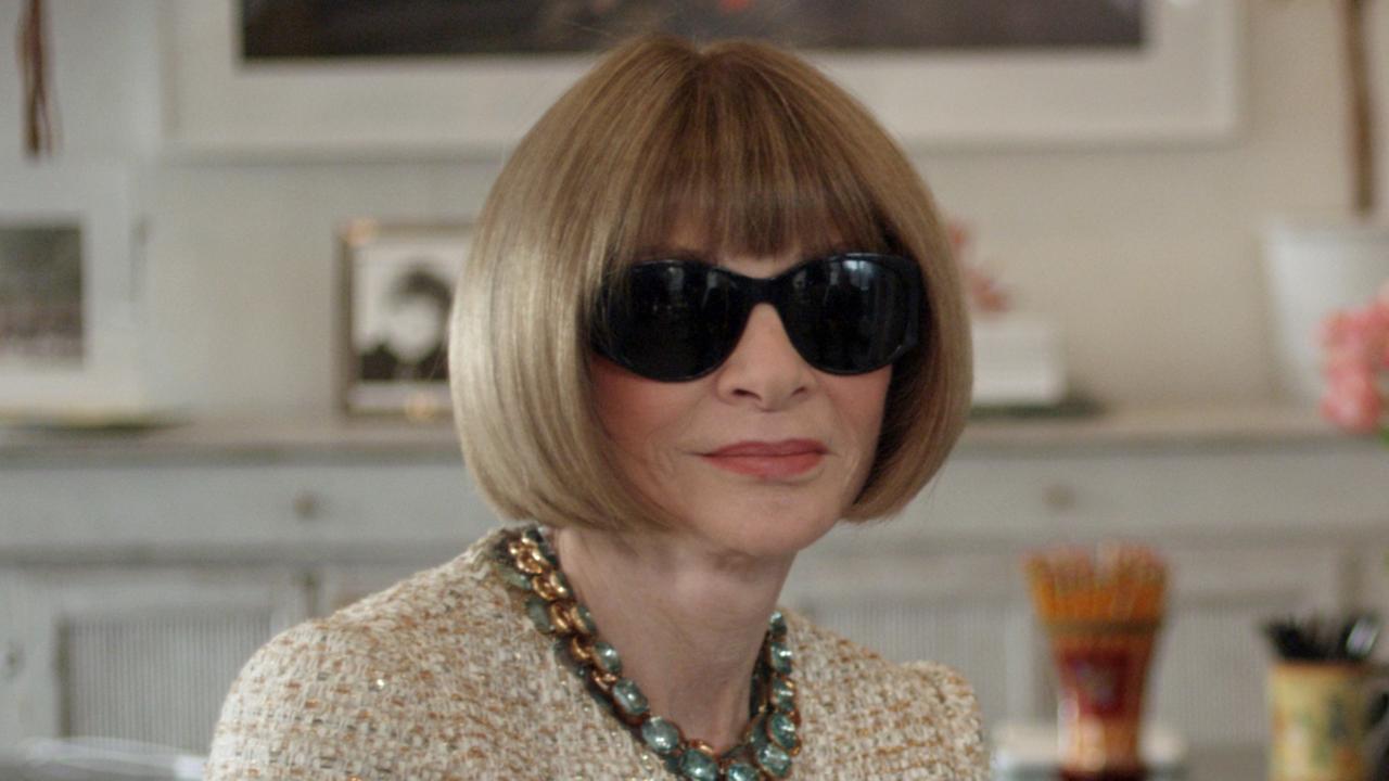 Das Bild zeigt Anna Wintour, die Chefin der amerikanischen Zeitschrift „Vogue“ sitzend in einer Interviewsituation. Sie trägt ein beigefarbenes Kostüm, eine große Sonnenbrille, eine dunkle, große Perlenkette und die für sie typische Bob-Frisur.