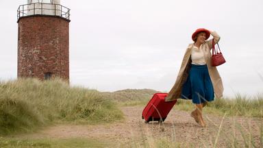 Auf der Insel Sylt läuft Inge (Gaby Dohm) an einem Leuchtturm vorbei. Sie zieht mit der rechten Hand einen Koffer hinter sich her und hält mit der anderen Hand ihren Hut auf dem Kopf fest.