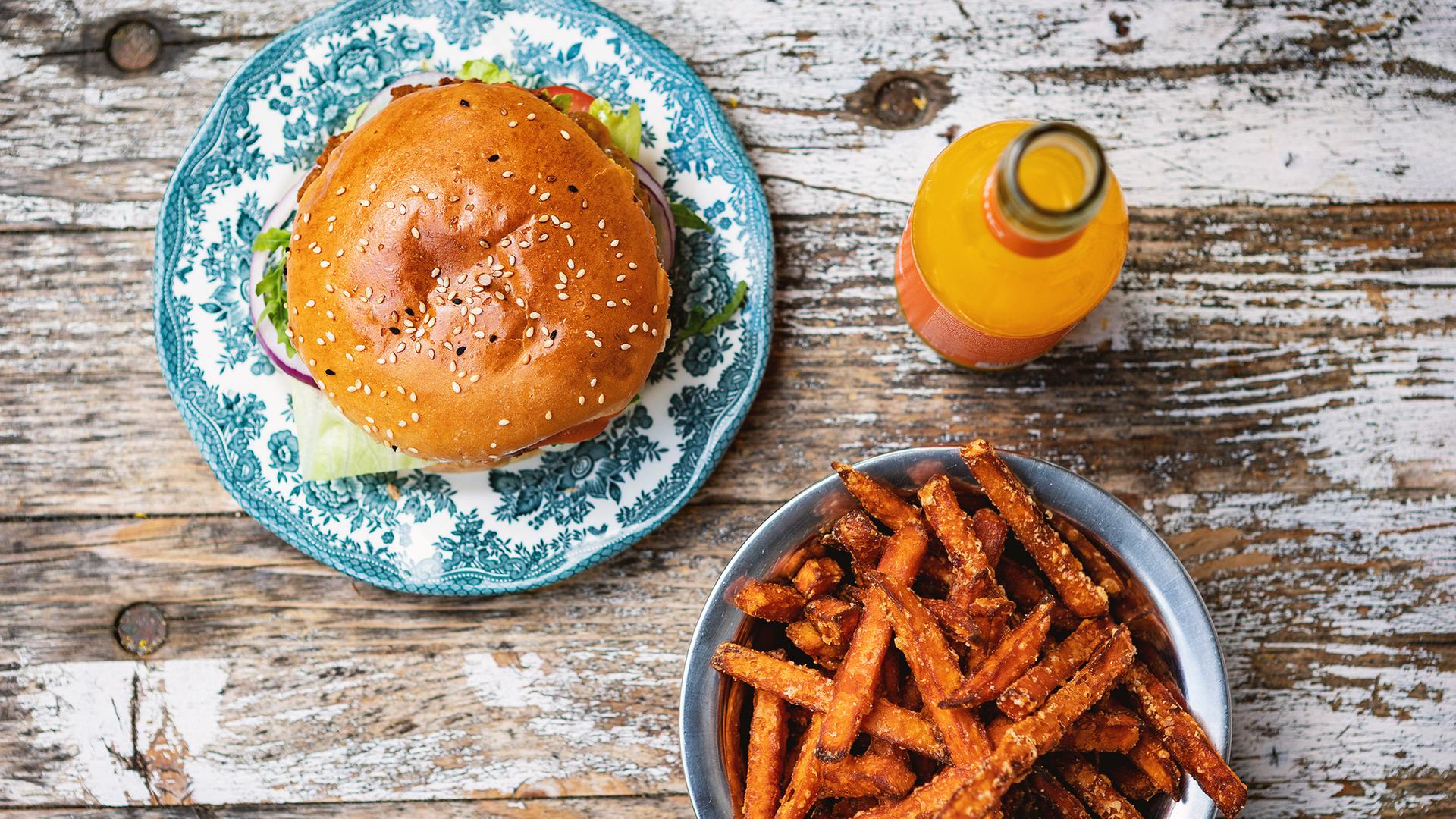 Ein Teller mit einem Burger neben einer Limonadenflasche und einer Schüssel mit Süßkartoffelpommes.