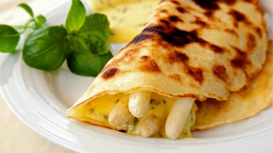Spargelstangen in einen Pfannkuchen eingerollt auf einem weissen Teller angerichtet