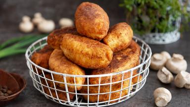 Kartoffelkrapfen in einem kleinen Körbchen. Im Hintergrund Pilze und Lauchzwiebeln.