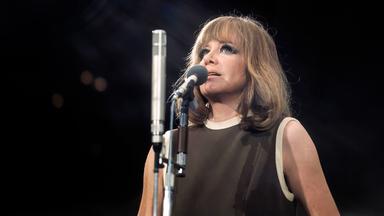 Eine Frau mit langen Haaren singt vor einem Mikrofon.