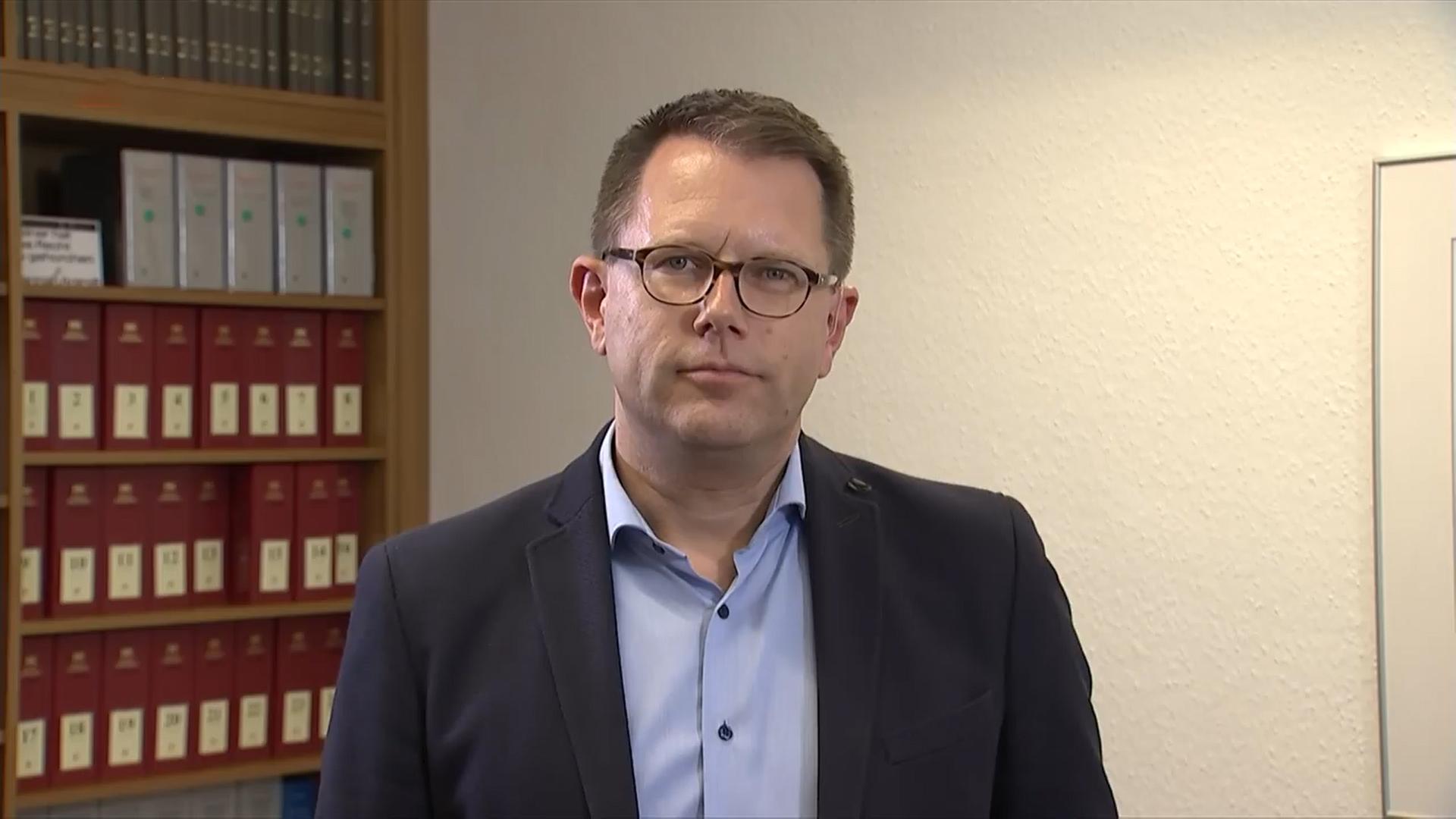 Ein Mann mit Brille sitzt vor einem Bücherregal.