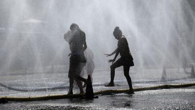 Die Silhouetten von drei Menschen sind zwischen Wassersprenklern zu sehen.
