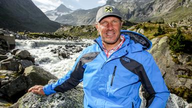 Mann in Outdoor-Kleidung vor einem Gebirgsbach