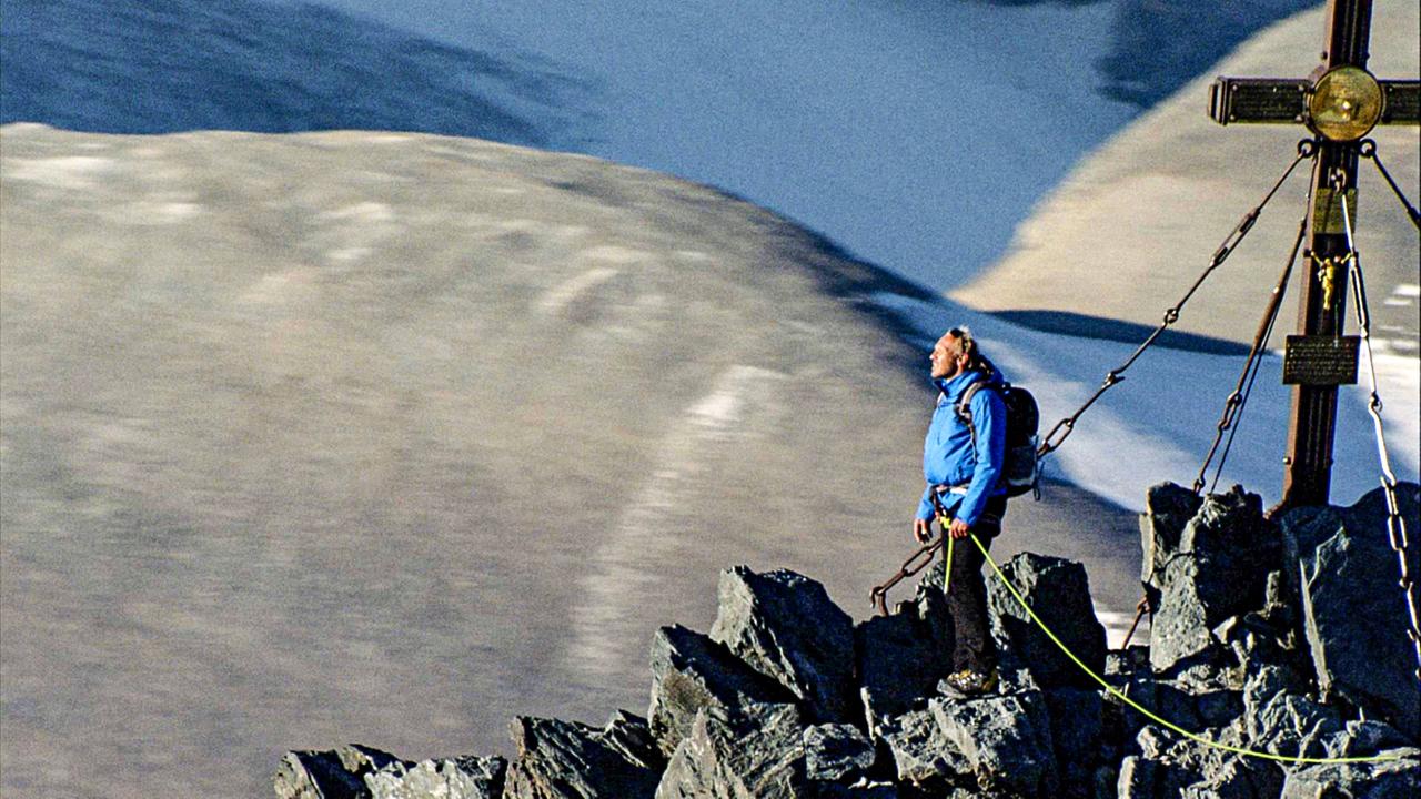 Ein Bergsteiger sonnt sich auf einem Gipfel neben dem Gipfelkreuz