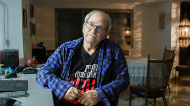 Mann sitzt seitlich an einem Schreibtisch mit einem geöffneten Laptop.