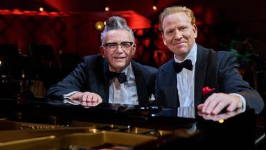 Götz Alsmann und Daniel Hope in identischen Jackets, Hemden und Fliegen sitzen lächelnd an einem Konzertflügel.