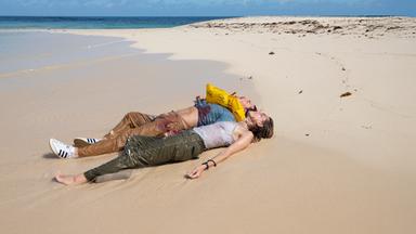 Sara (Allison Williams) und Jackson (Alexander Dreymon) liegen nebeneinander am Ufer einer Insel. Beide sind völlig erschöpft und haben die Augen geschlossen. Jackson trägt eine Schwimmweste, und an seiner Kleidung sind deutliche Blutflecken zu erkennen.