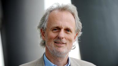 älterer Herr mit weißen Haaren und beigenem Anzug.