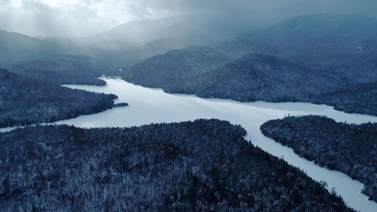 Zugefrorener See mit mehreren Zungen, umgeben von Wäldern