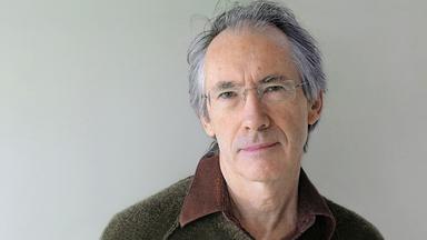 Ein Mann mit grauem Haar und und Pullover vor einem gräulichen Hintergrund