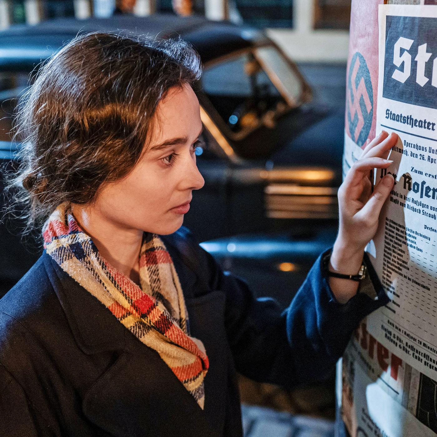 Junge Frau liest ein Plakat an einer Litfaßsäule.