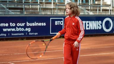 Mädchen im roten Trainingsanzug auf dem Tennisplatz