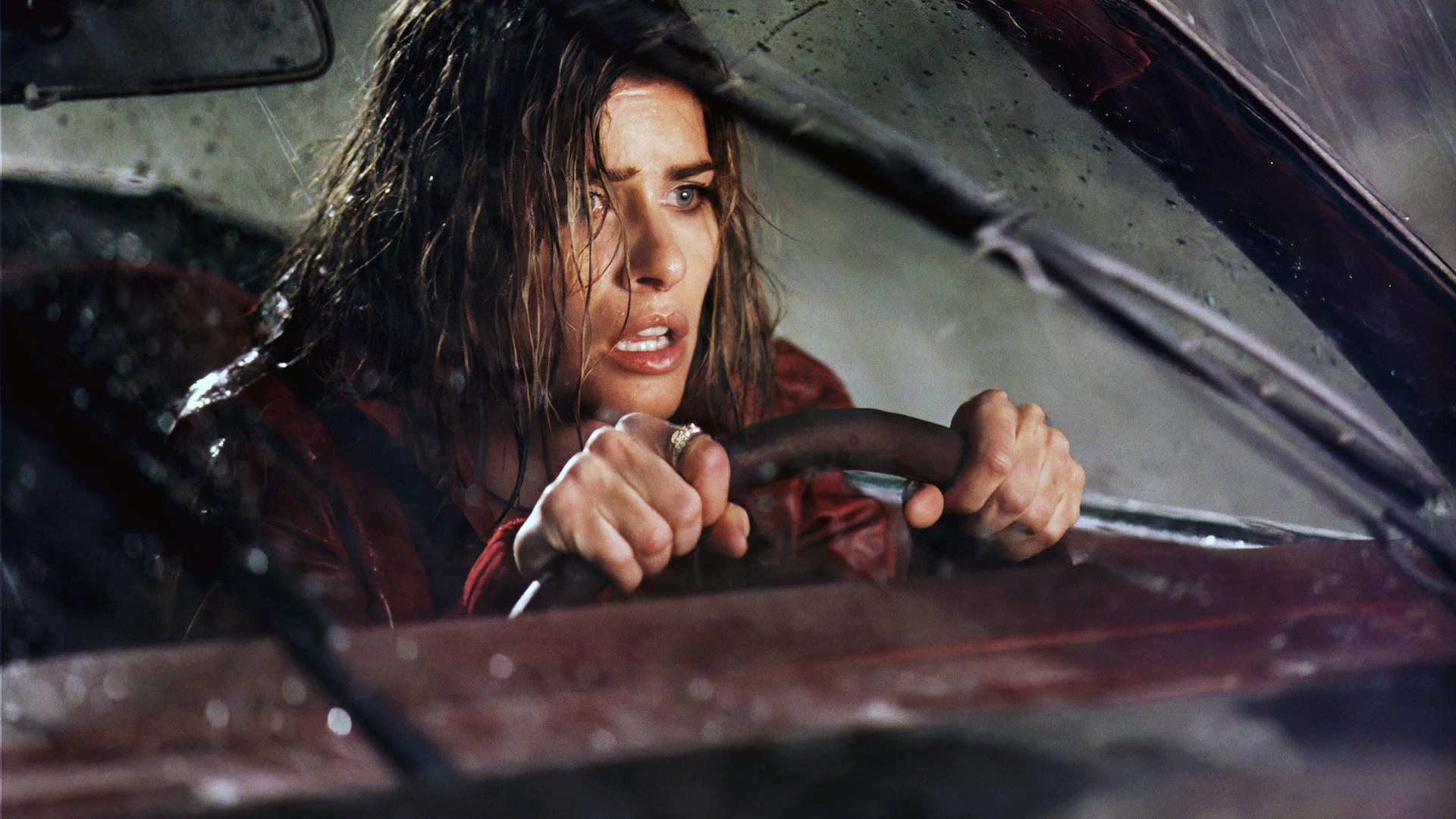 Eine nasse Frau sitzt nachts angespannt und konzentriert am Steuer eines Autos mit beschlagener Windschutzscheibe  Szene aus dem Film Identität.