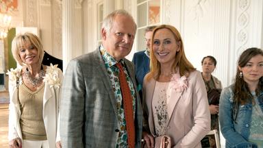 "Ihr seid natürlich eingeladen": Gundula (Andrea Sawatzki) und Gerald (Axel Milberg) schauen strahlend in die Kamera. Im Hintergrund ist der Rest der Familie zu sehen.