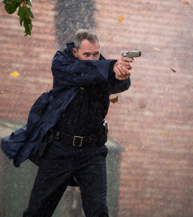 Sheriff Dixon (Ben Cross) steht mit erhobener Waffe im Freien und zielt auf jemanden außerhalb des Bildes. Um ihn herum tobt der Sturm.