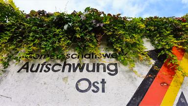 Ein verwitterter Anstrich mit dem Schriftzug "Aufschwung Ost" und den deutschen Nationalfarben, aufgenommen an einer Schallschutzwand in Magdeburg.