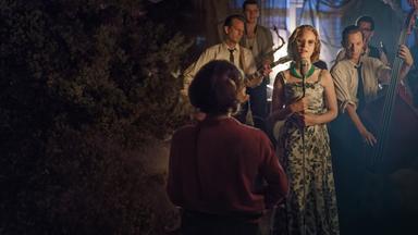 Monika Schöllack (Sonja Gerhardt) steht auf einer Bühne und singt, während Freddy Donath (Trystan Pütter) etwas hinter ihr Kontrabass spielt. Weitere Musiker stehen hinter den beiden.