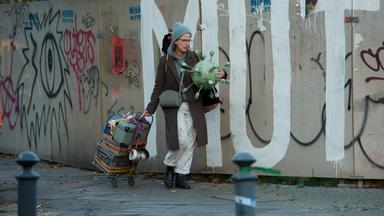 "Immer der Nase nach": Die Schaufensterdekorateurin Tanja (Claudia Michelsen) läuft mit Requisiten bepackt auf einer Straße, die an einem Bauzaun entlang führt. Der Zaun ist mit Graffiti besprüht. "Mut" ist in großen Lettern zu lesen.